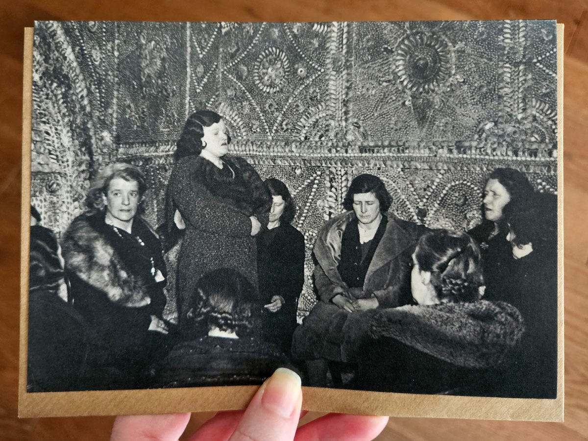 A hand holding a gift card featuringa black and white image of women sitting and standing in a circle A hand holding a gift card featuringa black and white image of women sitting and standing in a circle