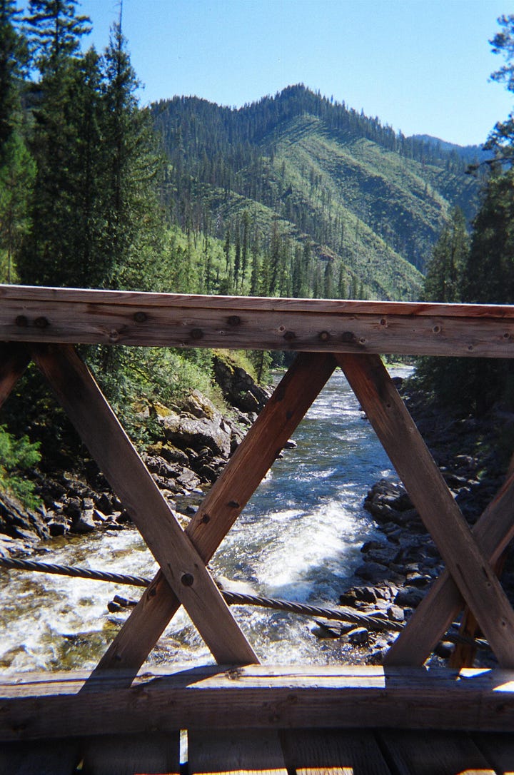 Two men on a mountaintop, a bridge over a creek, a backpack with tools, a waterfall.