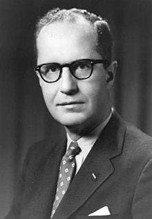 A person wearing glasses and a suit

Description automatically generated