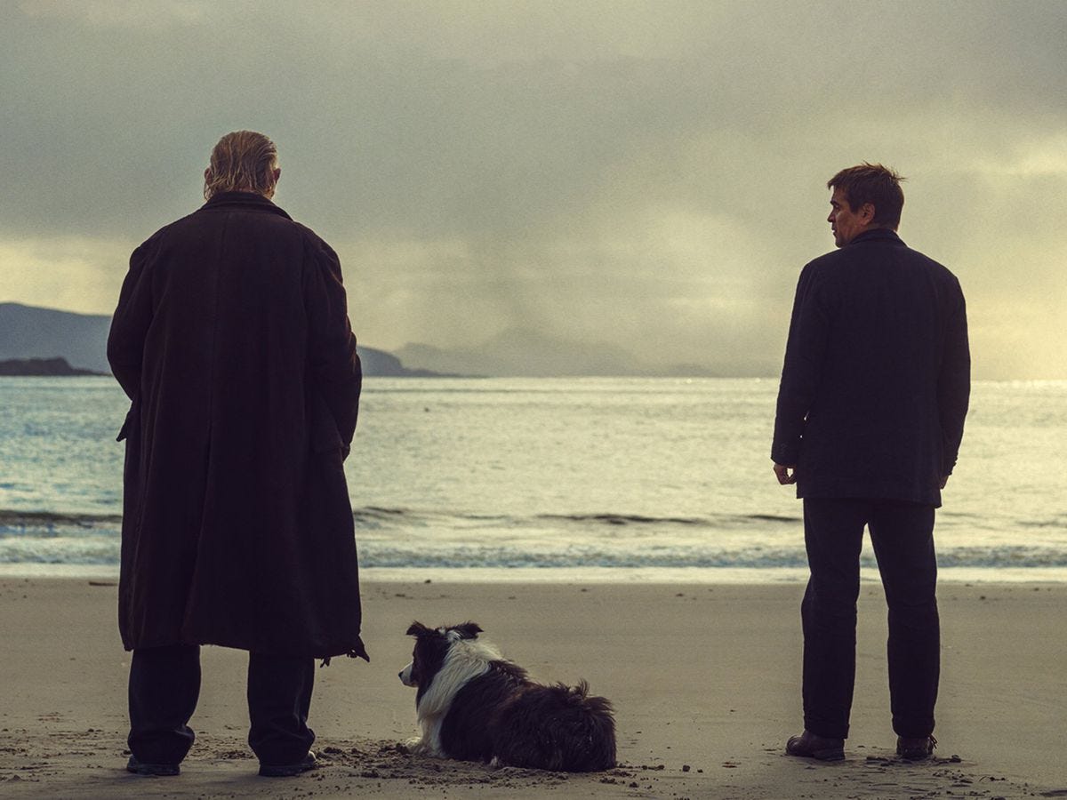 Two men face the water, away from the camera. One looks at the other.