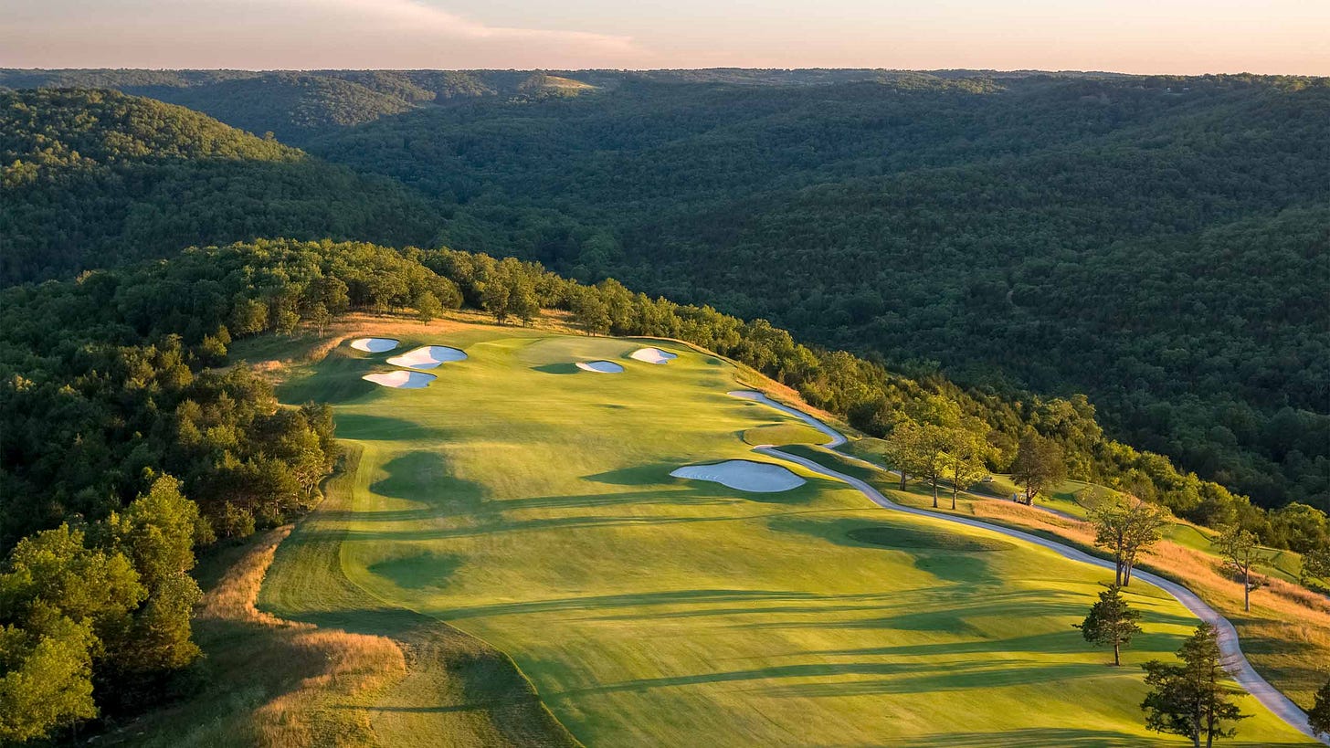 Aerial view of Payne's Valley Golf Course showing lush green fairways, white sand bunkers, and a winding cart path set against a backdrop of densely forested Ozark Mountains at sunset. Aerial view of Payne's Valley Golf Course showing lush green fairways, white sand bunkers, and a winding cart path set against a backdrop of densely forested Ozark Mountains at sunset.