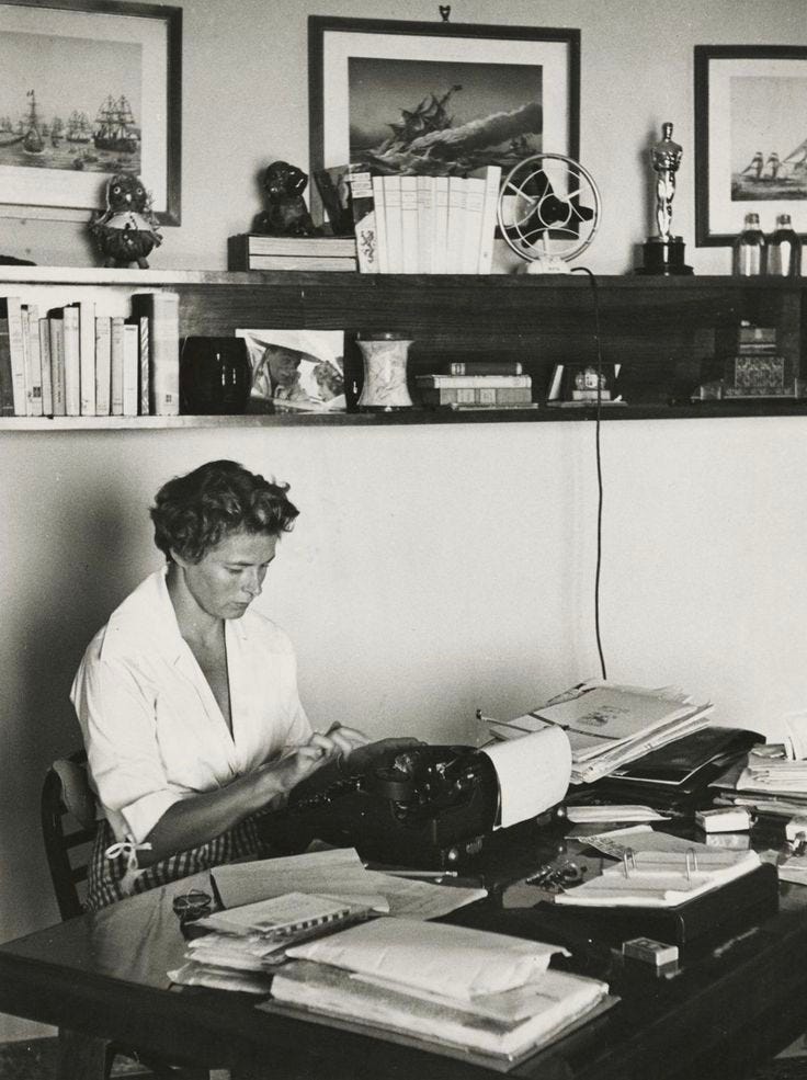 This may contain: a woman sitting at a desk working on an old typewriter in her home office