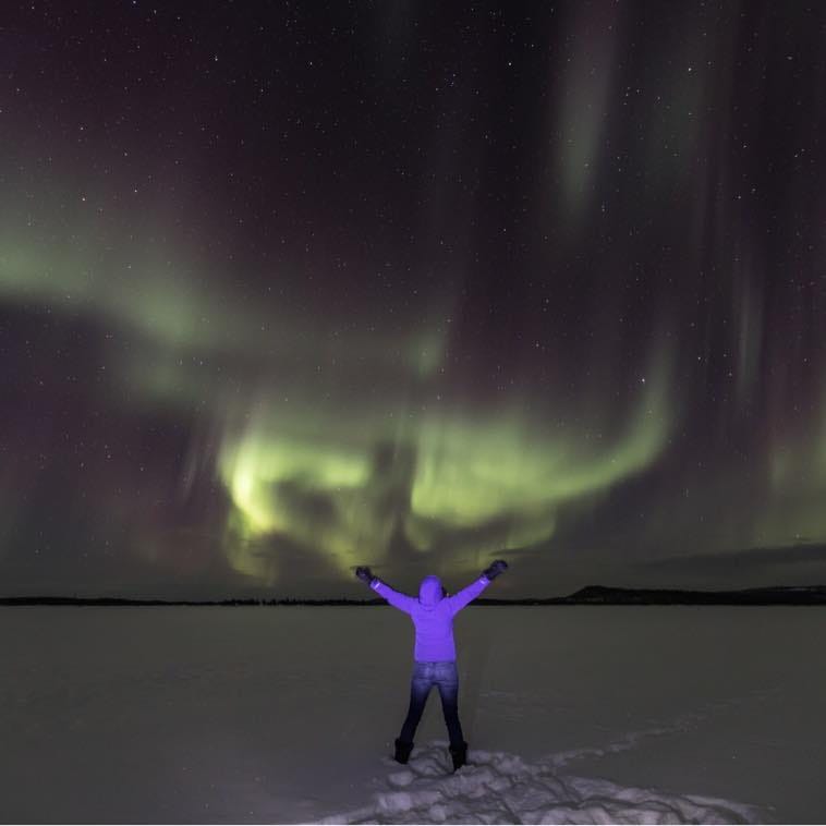 Jenny under northern lights, arms outstretched.