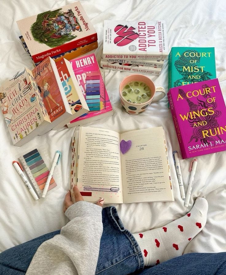 This may contain: a person laying on a bed with books and other items in front of them,