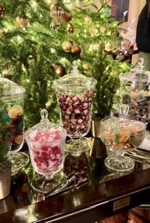 A table of colourful sweets in jars and a small mince pie in front of an open fire.