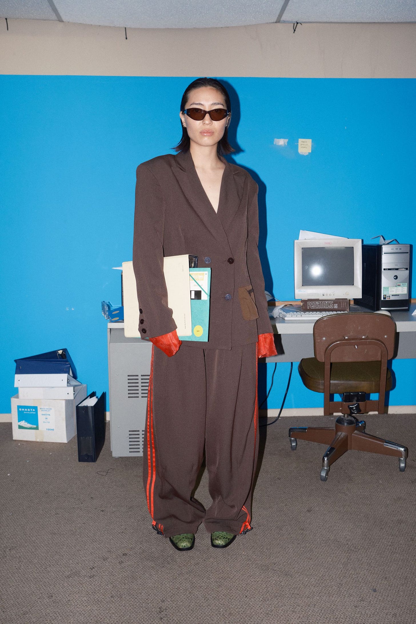 Image may contain Person Standing Chair Furniture Accessories Glasses Blazer Clothing Coat Jacket Adult and Table