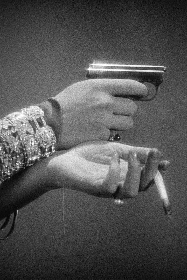 Black and white close-up of a a woman's hands. She holds a pocket gun in her right hand, aiming at something out of a frame, and a cigarette dangles from the left one. She wears several diamond bracelets and two big gem rings.