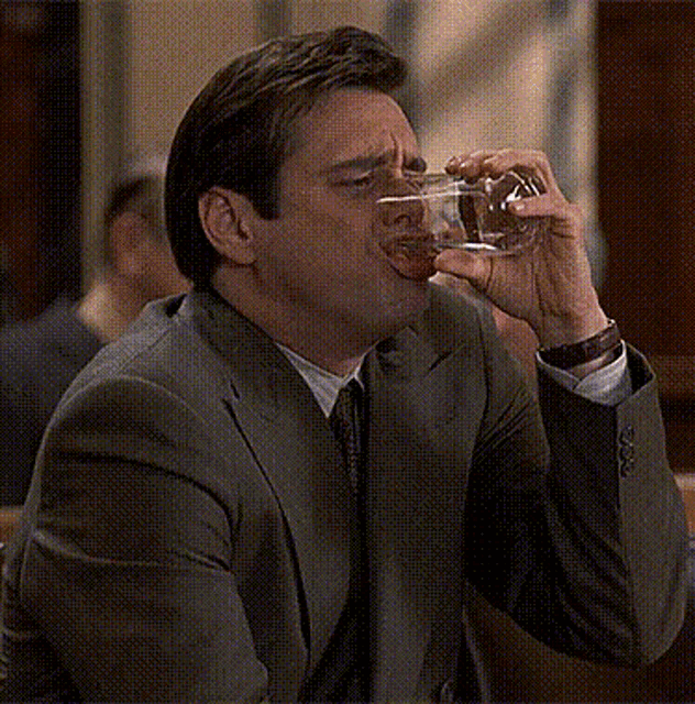 a man in a suit is drinking from a clear glass