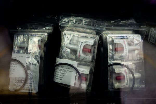 A close view of a row of Narcan nasal sprays are packaged in plastic sealed bags, two per bag, behind the glass of a vending machine.