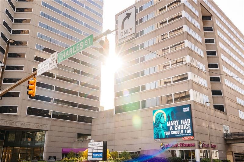 The billboard shows Mary, Mother of God, in profile, with the bishops looming behind her. The text of the billboard reads, "Mary Had a Choice. You Should Too."