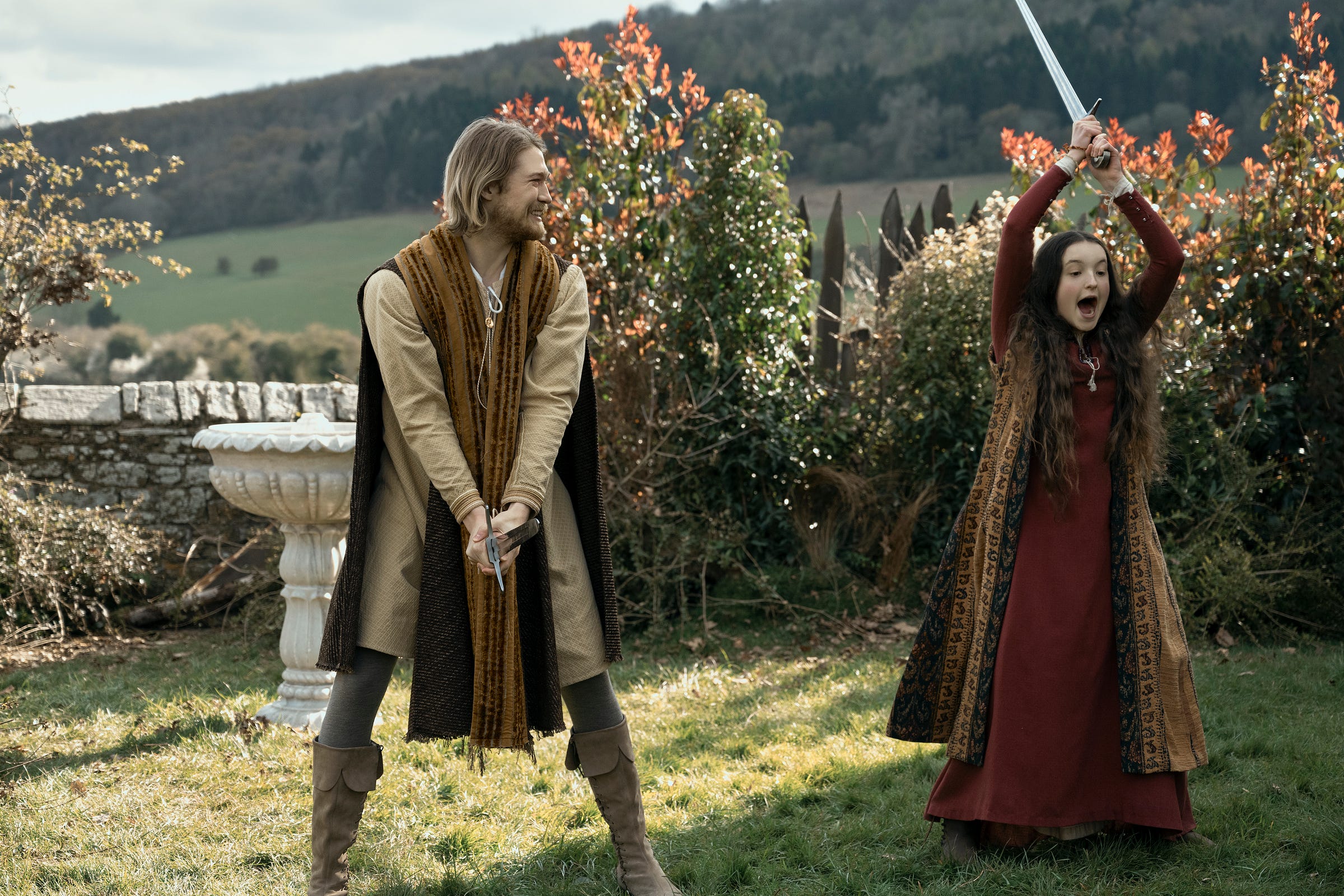 Catherine (Bella Ramsey) swinging her sword wildly with her mouth open while her uncle (Joe Alwyn) looks on