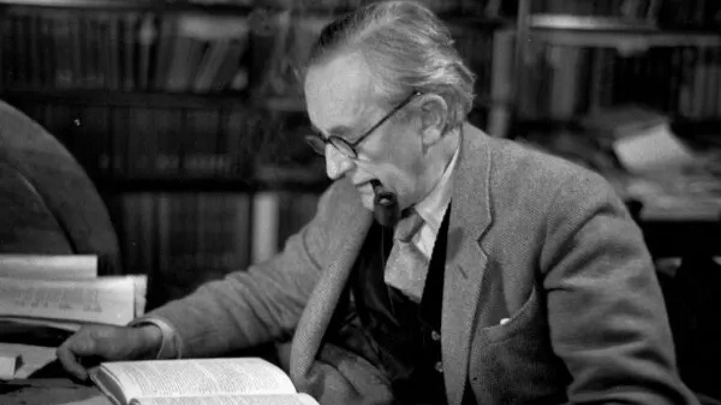 JRR Tolkien looks down at desk with pipe in mouth