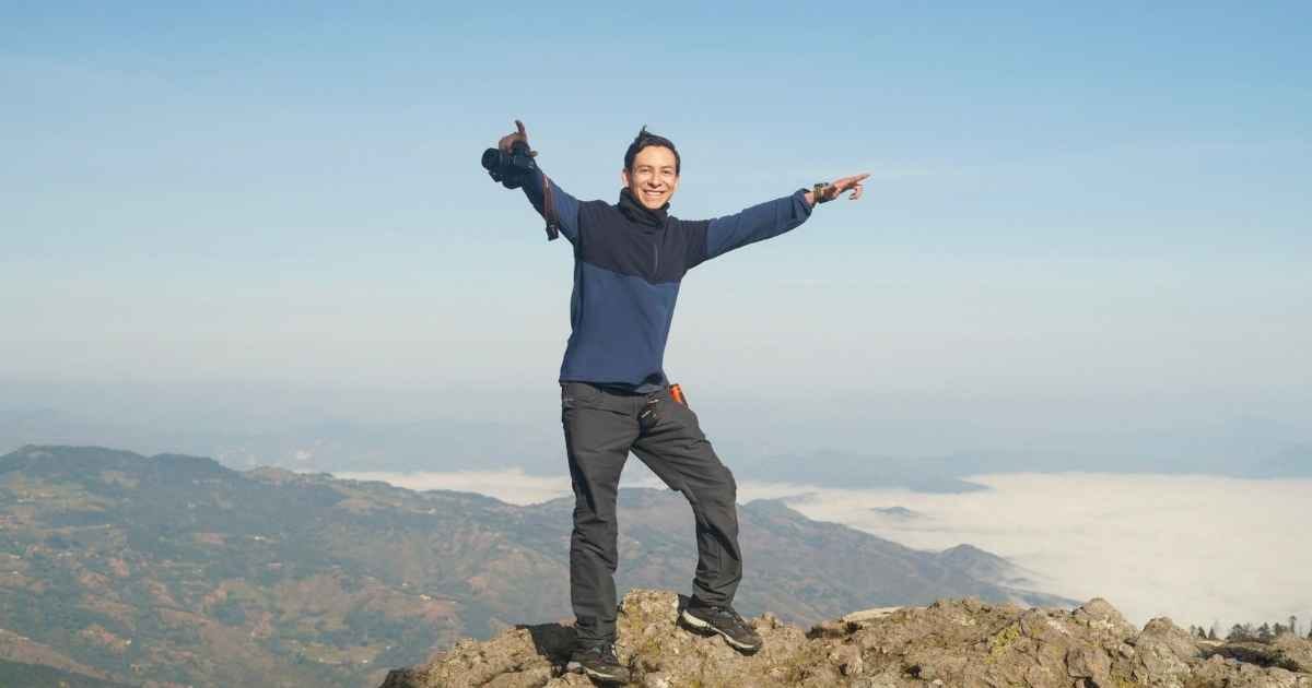Joyful man standing on mountain peak with breathtaking landscape views. Adventure and freedom concept Joyful man standing on mountain peak with breathtaking landscape views. Adventure and freedom concept
