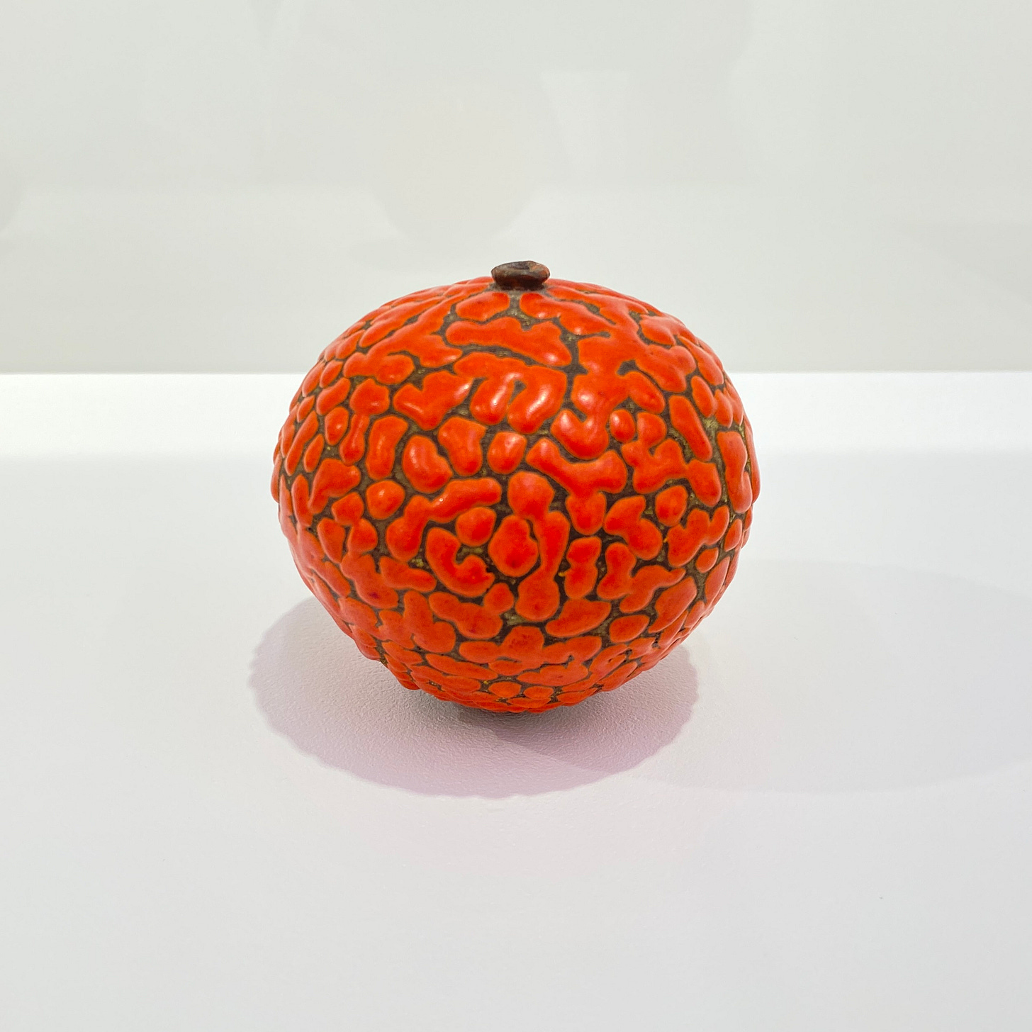 A close up view of a single weed pot, covered evenly with curving islands of brilliant red glaze. The pot is generously rounded, wider near the top and somewhat narrower at the base. It has a tiny lip of bare clay at the opening.
