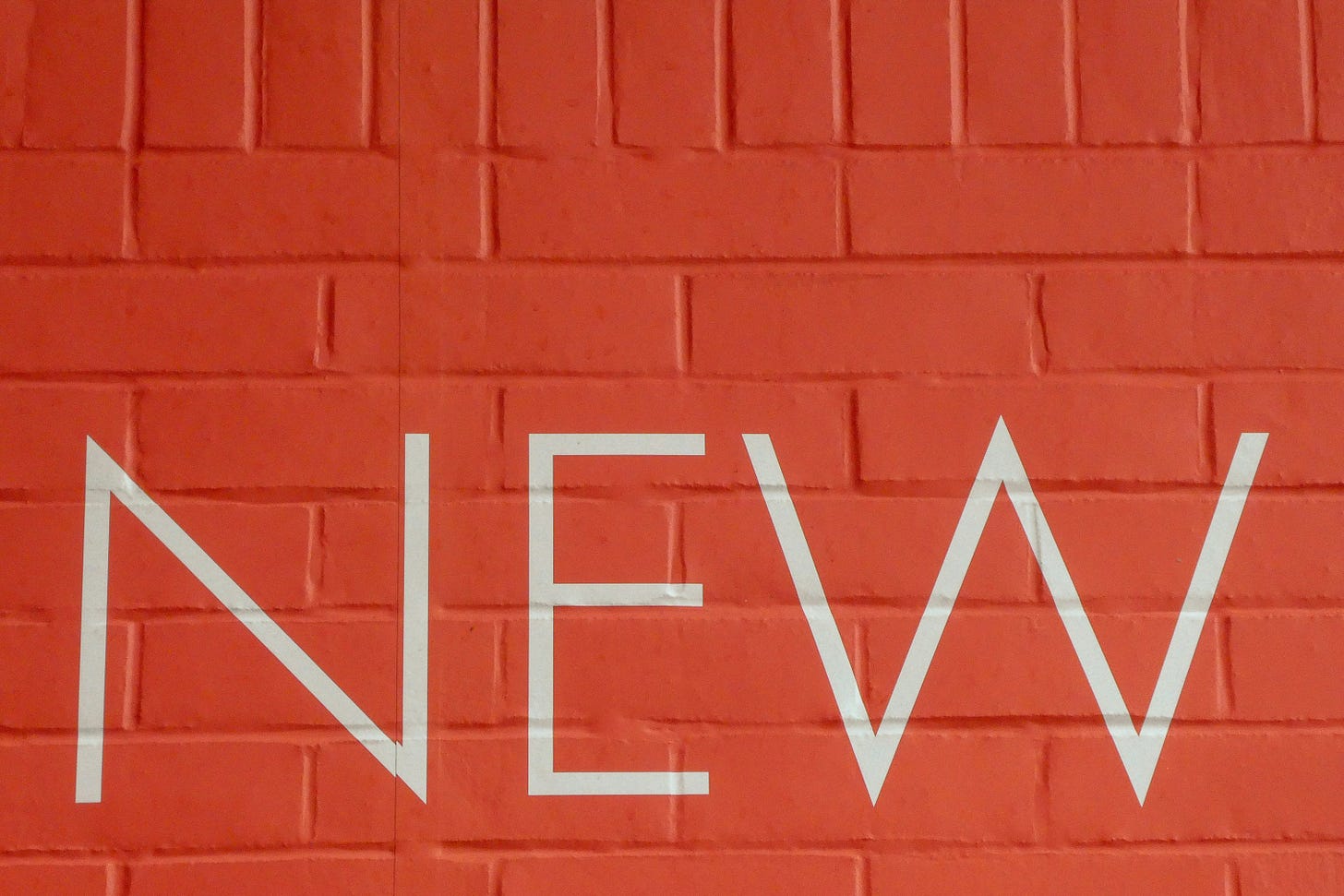 The word New, painted in white in block capitals on a red painted brick wall The word New, painted in white in block capitals on a red painted brick wall
