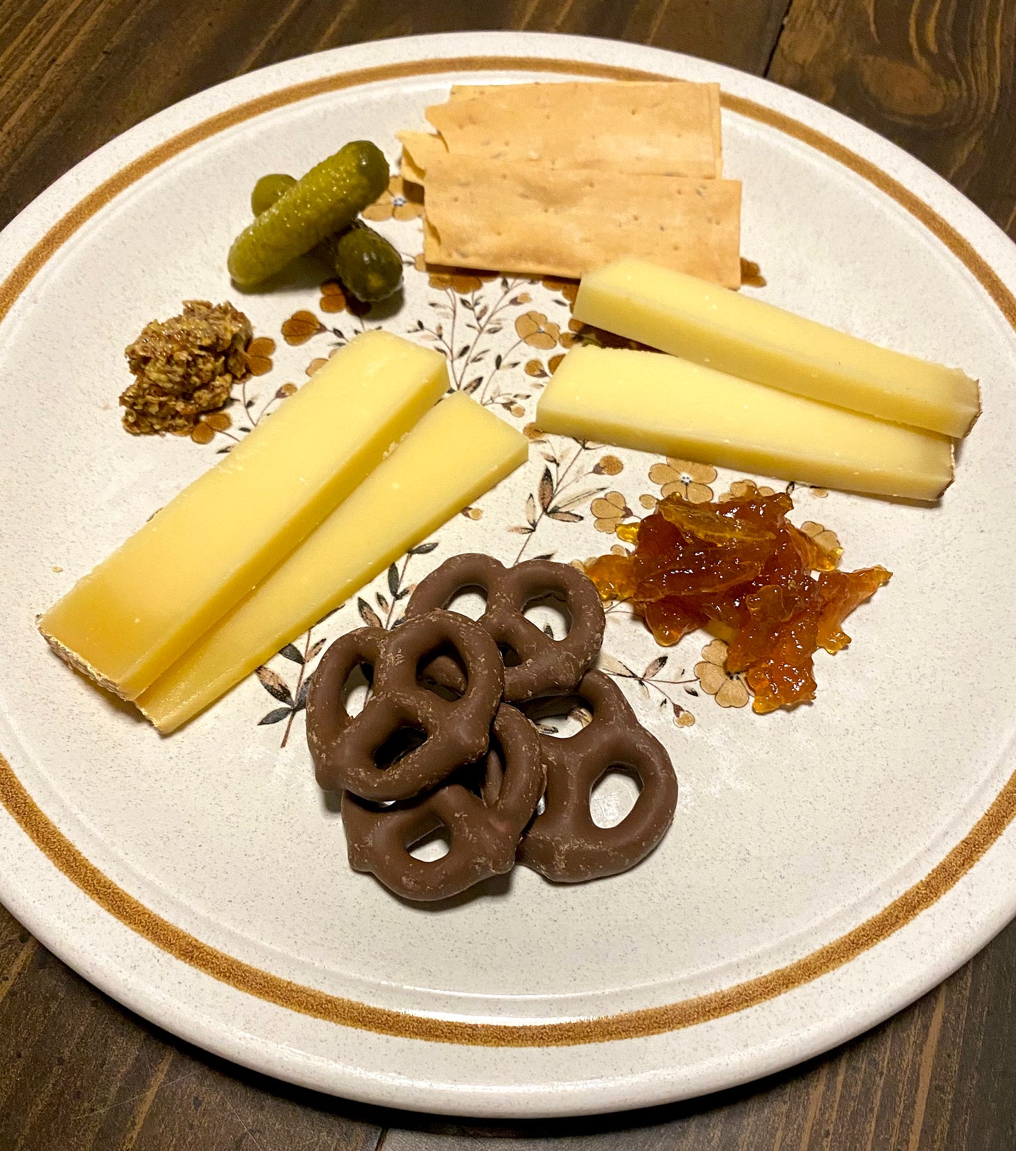 cheese tasting plate with gruyere, mustard, cornichon, thyme crackers, comte, lemon marmalade, and chocolate covered pretzels