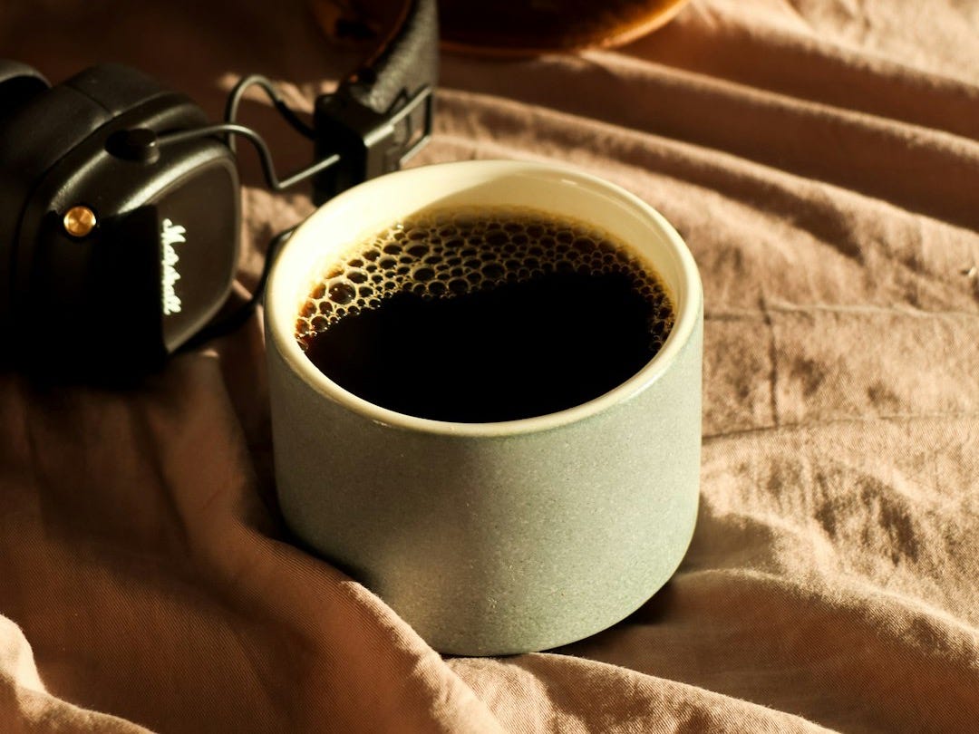 Cup of coffee and headphones on a bed.