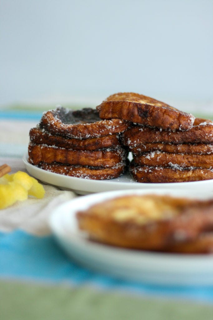 Traditional Spanish torrijas fried in olive oil and covered in sugar, and a beautiful stack of torrijas in the background