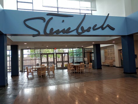 Museum building exterior, lobby with large sign "Steinbeck:, and entrance with statue of seated Steinbeck peeking out