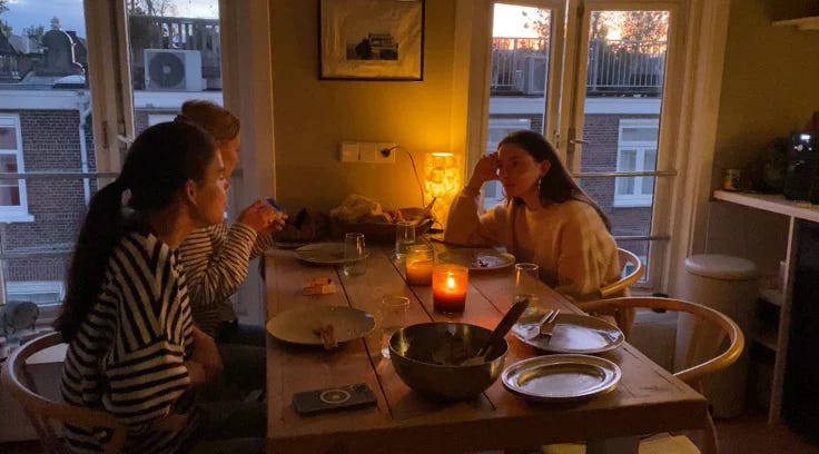 This may contain: two women sitting at a table with food in front of them and candles on the windows This may contain: two women sitting at a table with food in front of them and candles on the windows