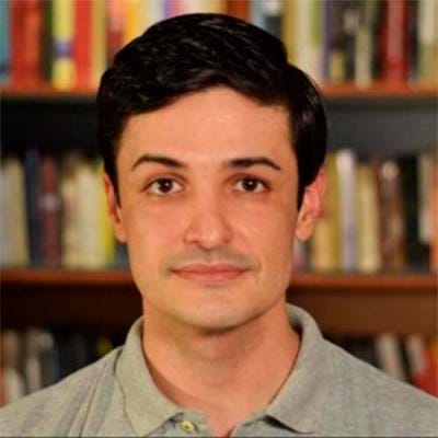 Homem branco, cabelos pretos e curtos, usando camisa cinza