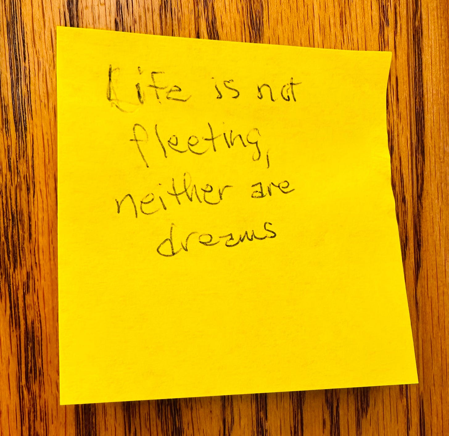 Yellow sticky note on a wood surface with the words "Life is not fleeting, neither are dreams"