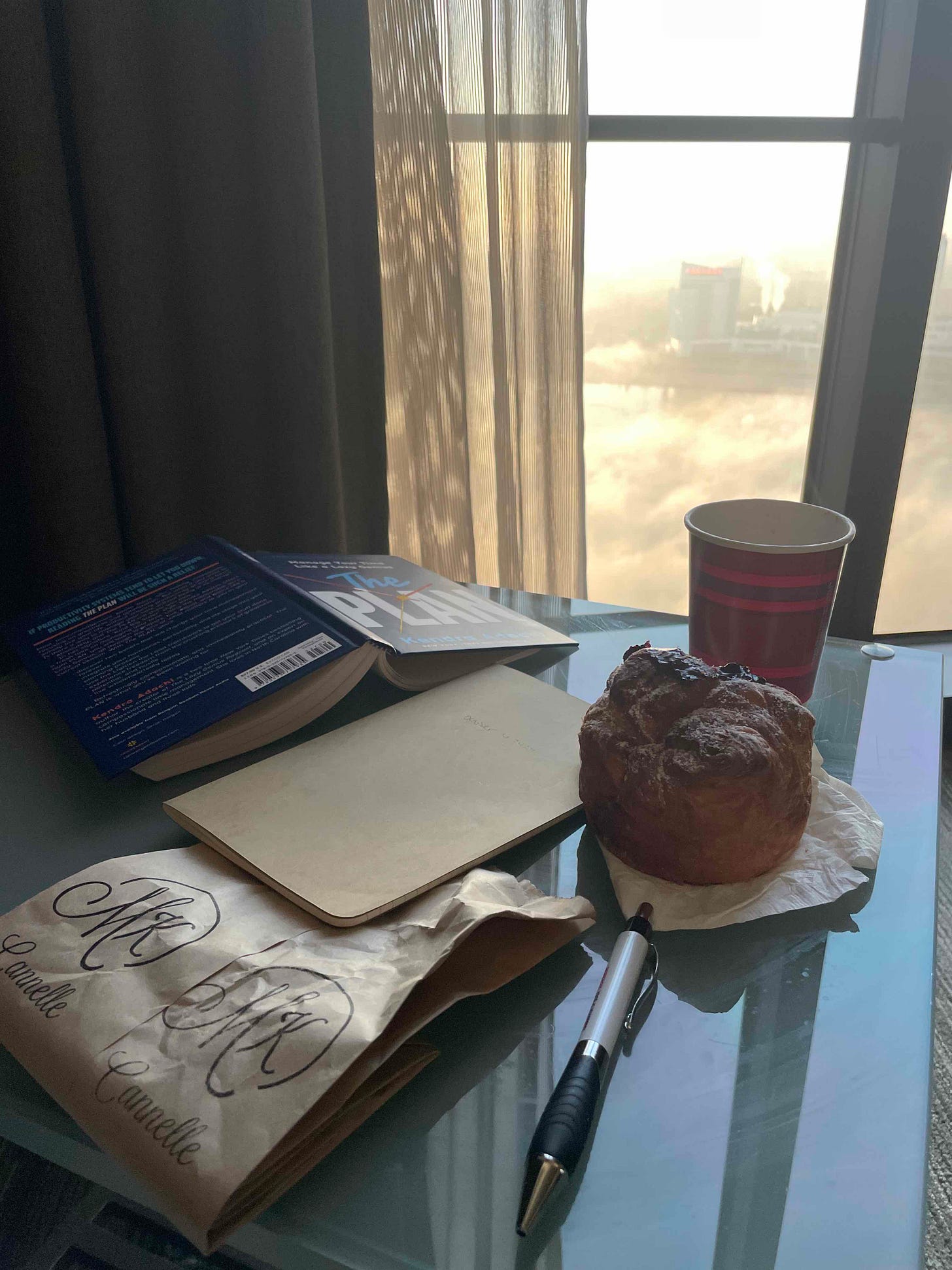 a book, a journal, a pastry on a table next to a window