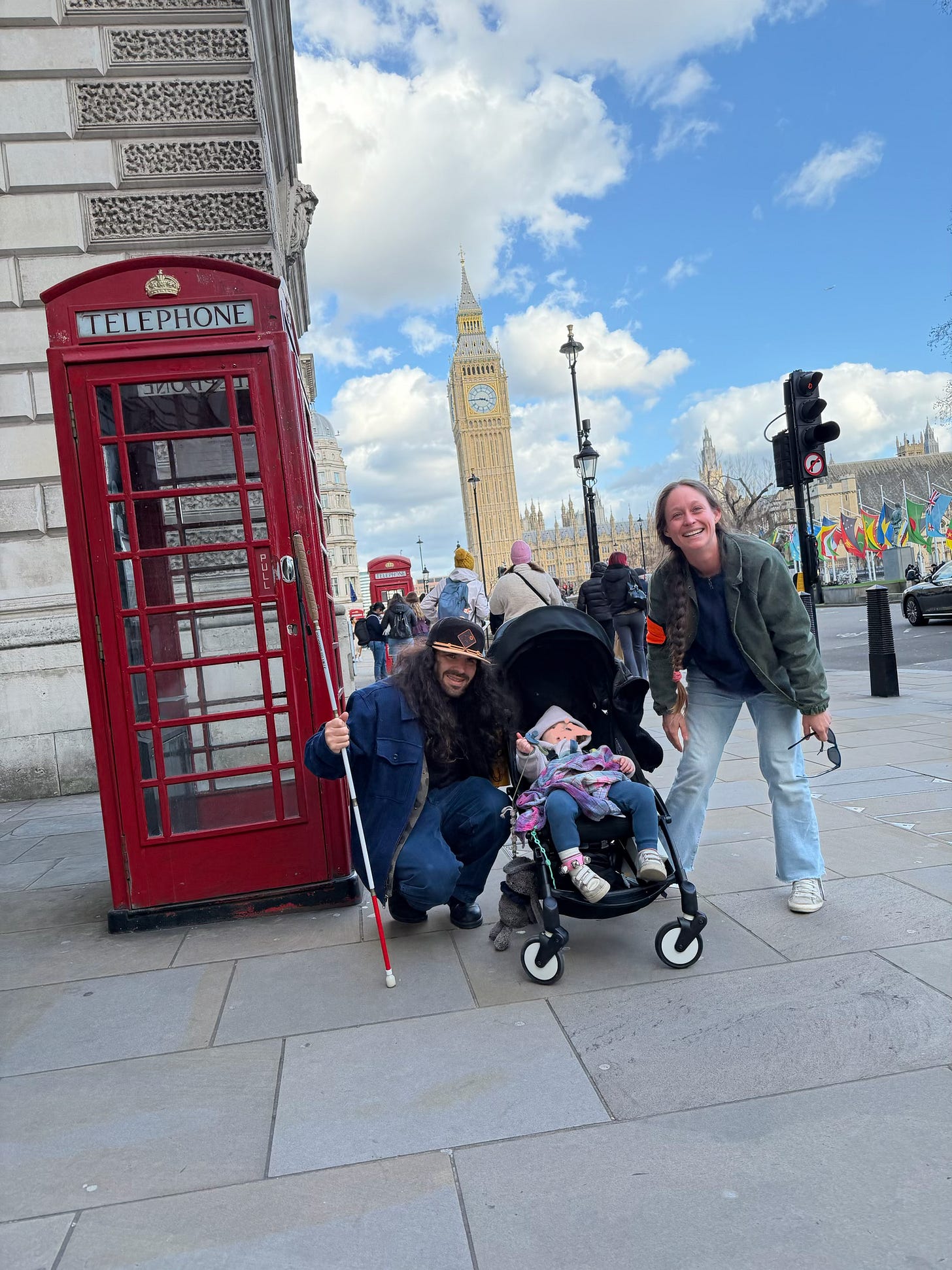 anthony, kelly and their daughter pose in front of a classic red telephone booth in London with Big Ben in the background