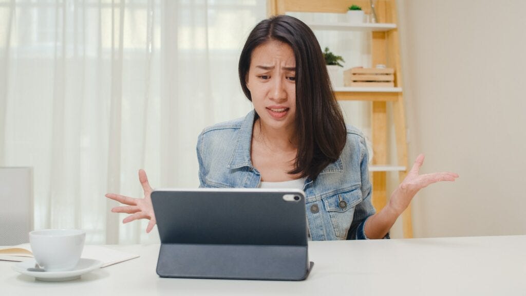Frustrated Young Asia lady having problem with not working tablet computer sitting on desk. Frustrated Young Asia lady having problem with not working tablet computer sitting on desk.