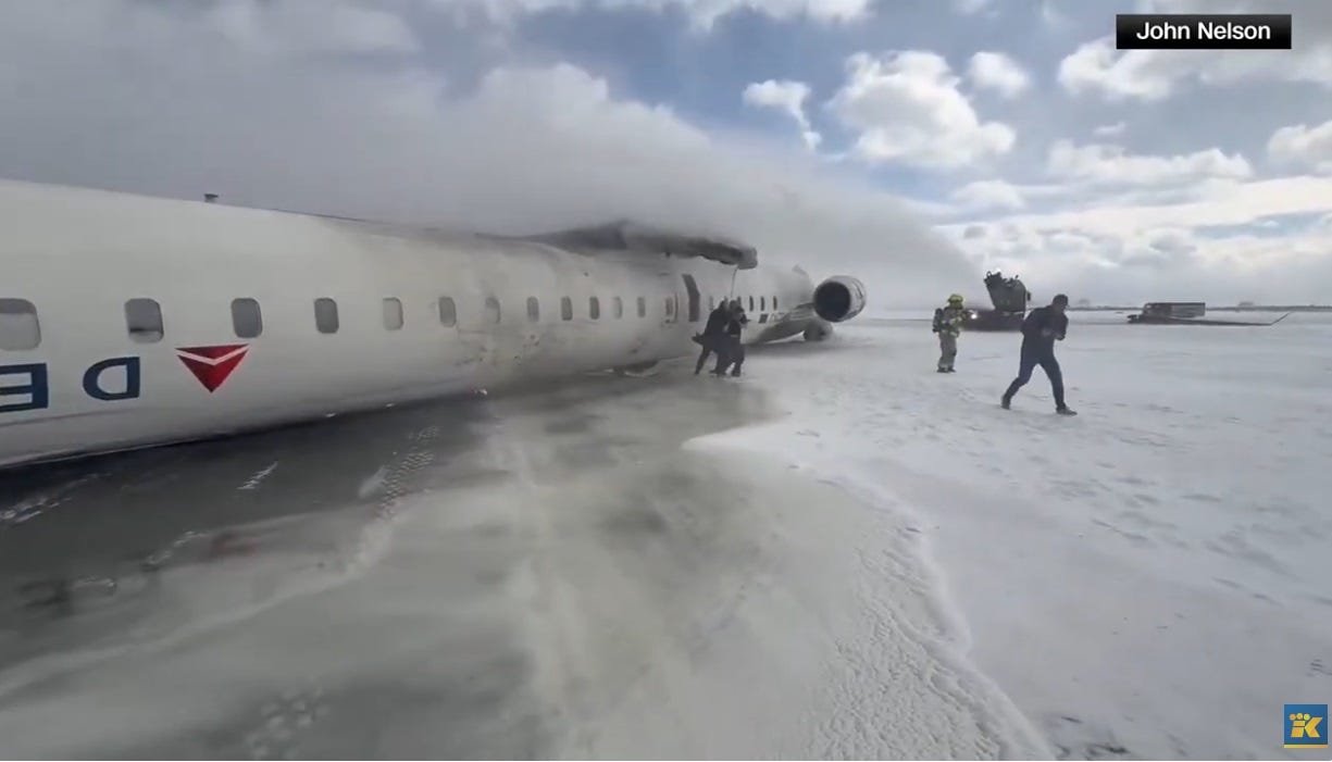 video screenshot of upside down jet plane on runway; the Delta logo toward the front, jagged root of wing in center of fuselage. Passengers are still escaping the plane as it's being sprayed with foam by a fire truck. On right side of photo can be seen the wing that broke off when plane landed, causing it to flip. video screenshot of upside down jet plane on runway; the Delta logo toward the front, jagged root of wing in center of fuselage. Passengers are still escaping the plane as it's being sprayed with foam by a fire truck. On right side of photo can be seen the wing that broke off when plane landed, causing it to flip.