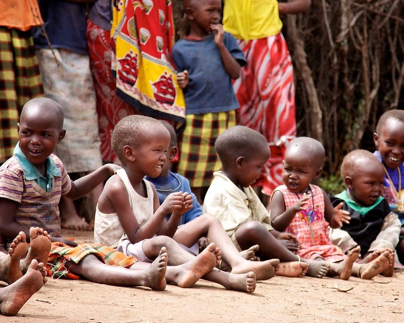 Several young children seated on the ground while laughing and smiling. Several young children seated on the ground while laughing and smiling.
