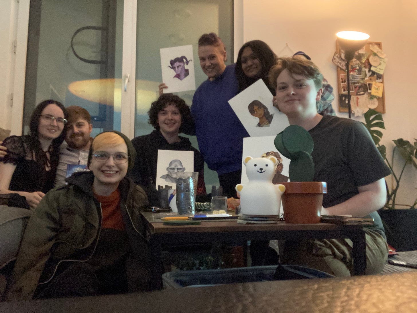 Beck sitting on the floor with six other humans around a coffee table covered in dungeons and dragons figures. Four are holding up pictures of their characters, including a tiefling warlock and a stone goliath