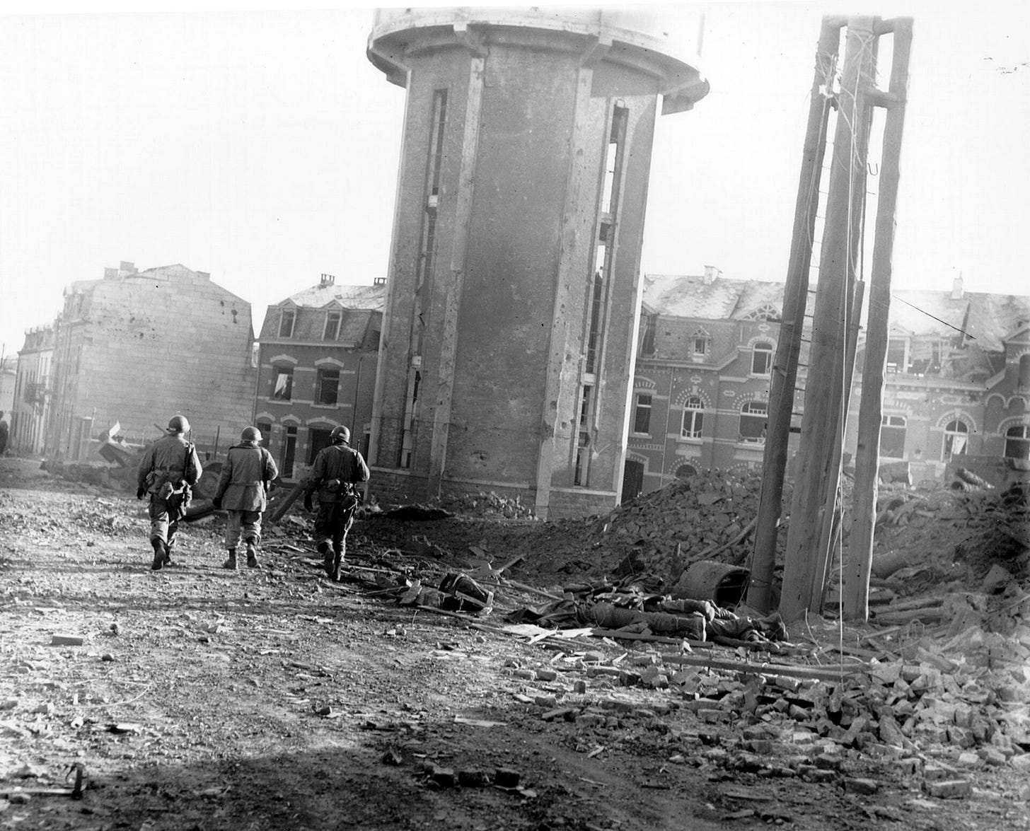 Black and white photo of soldiers walking through ruined buildings and rubble.