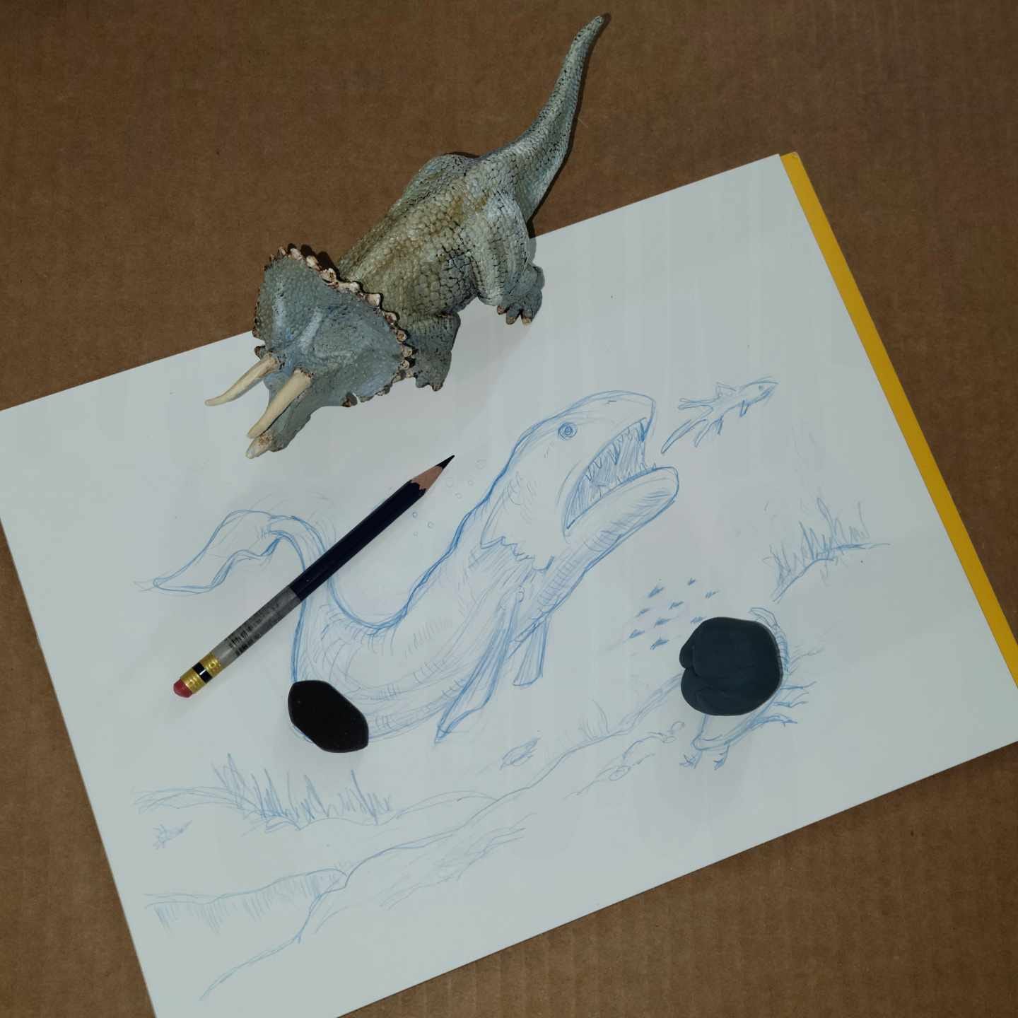 Image of a pencil drawing of an ancient fish with a pencil, eraser, and little toy triceratops on top of the paper. Image of a pencil drawing of an ancient fish with a pencil, eraser, and little toy triceratops on top of the paper.
