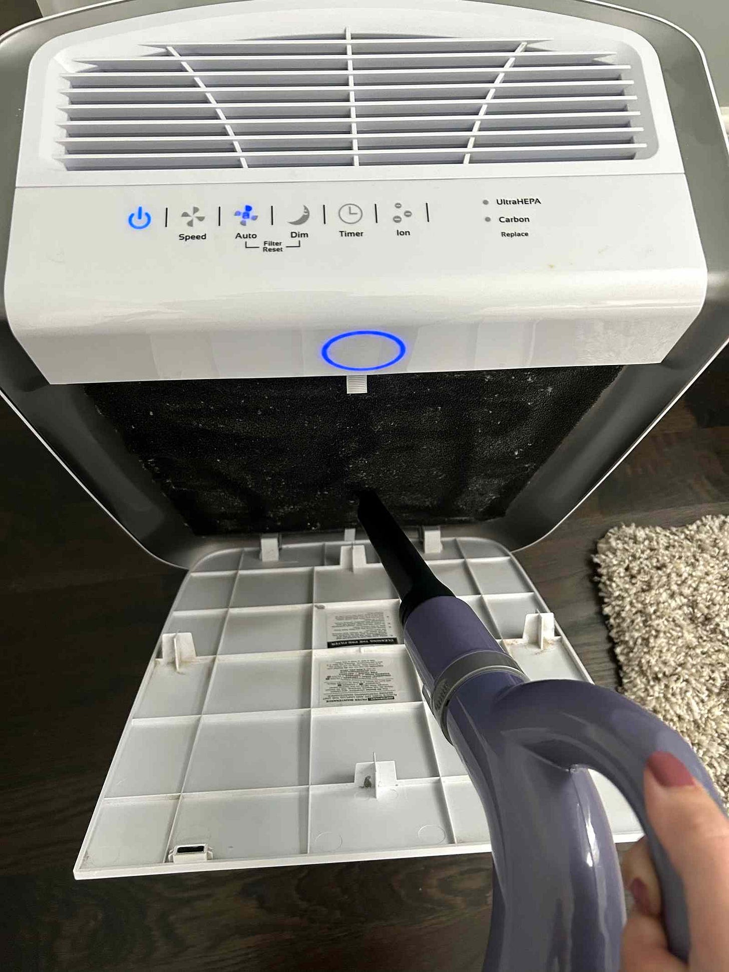 A handheld vacuum cleaning the open filter of an AirDoctor, panel lit blue A handheld vacuum cleaning the open filter of an AirDoctor, panel lit blue