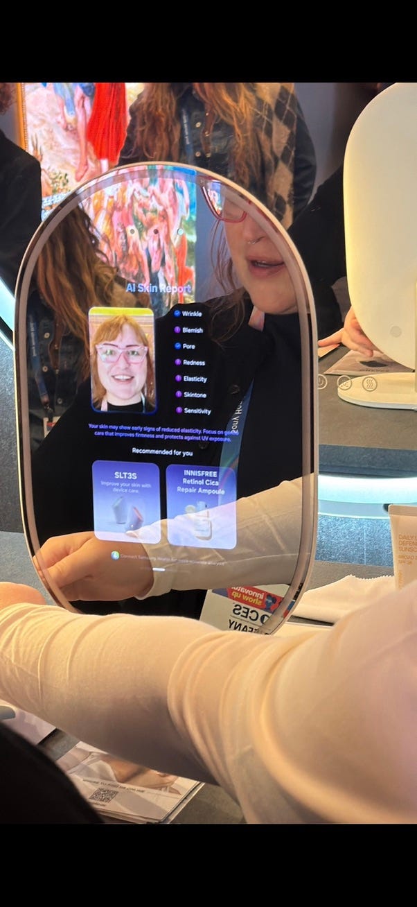 A Samsung AI Mirror displays a digital analysis of a person’s face, showing recommended makeup shades and best-fit colors. Another frame the mirror presents a skin analysis panel with categories like wrinkles, pores, redness, and elasticity. The person’s reflection appears behind the diagnostic overlay while they interact with the device. The reflection of the person smiling is visible behind the transparent interface.