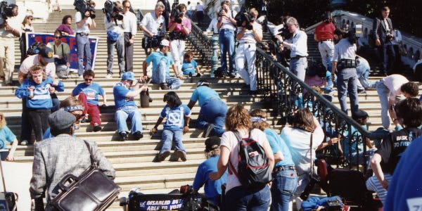 A photo of the Capitol Crawl, picturing a diverse group of disabled people crawling up the Capitol steps as protest.