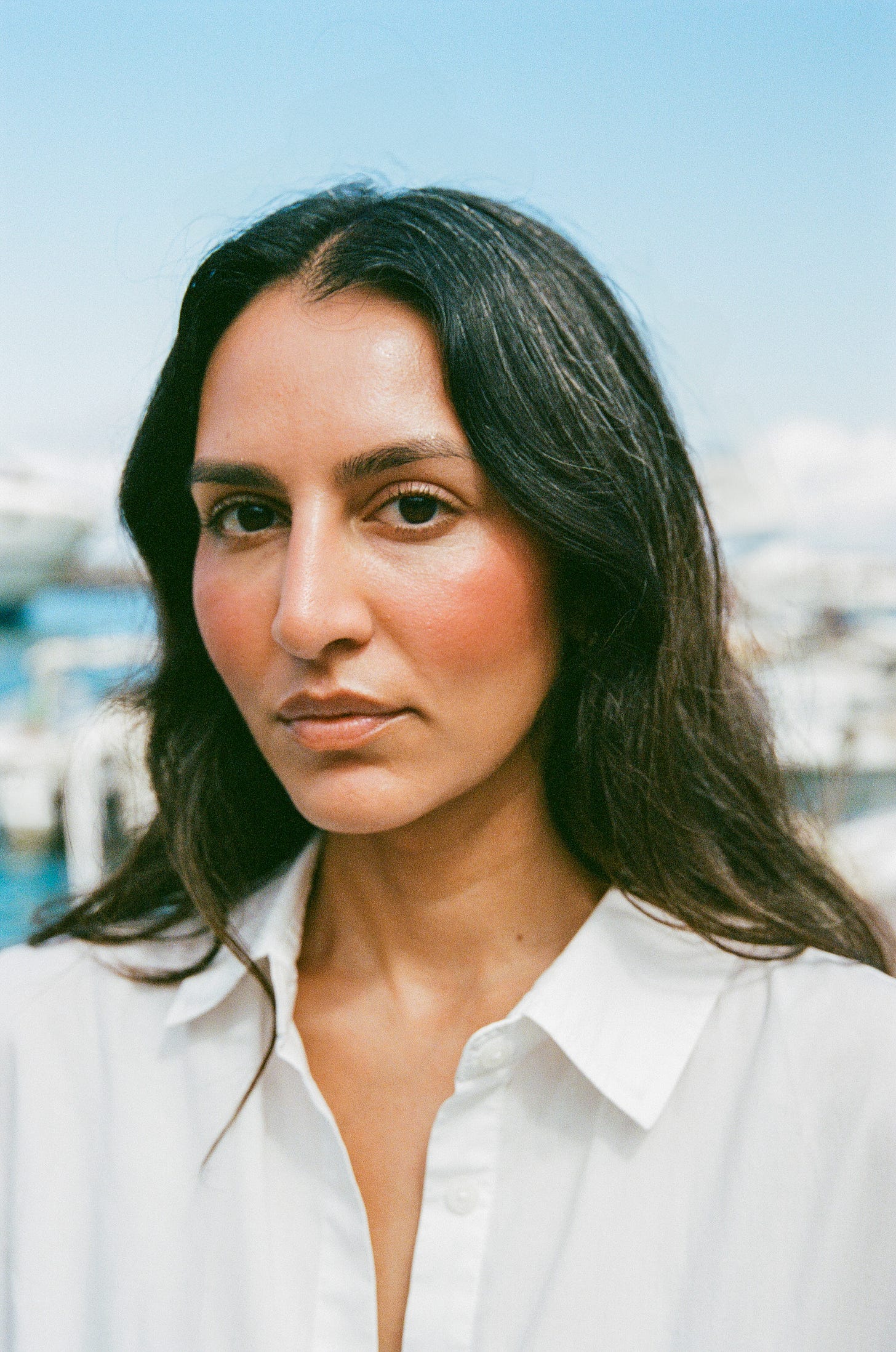 A portrait of a women wearing a white blous, with soft waves and bright blush on her cheeks.