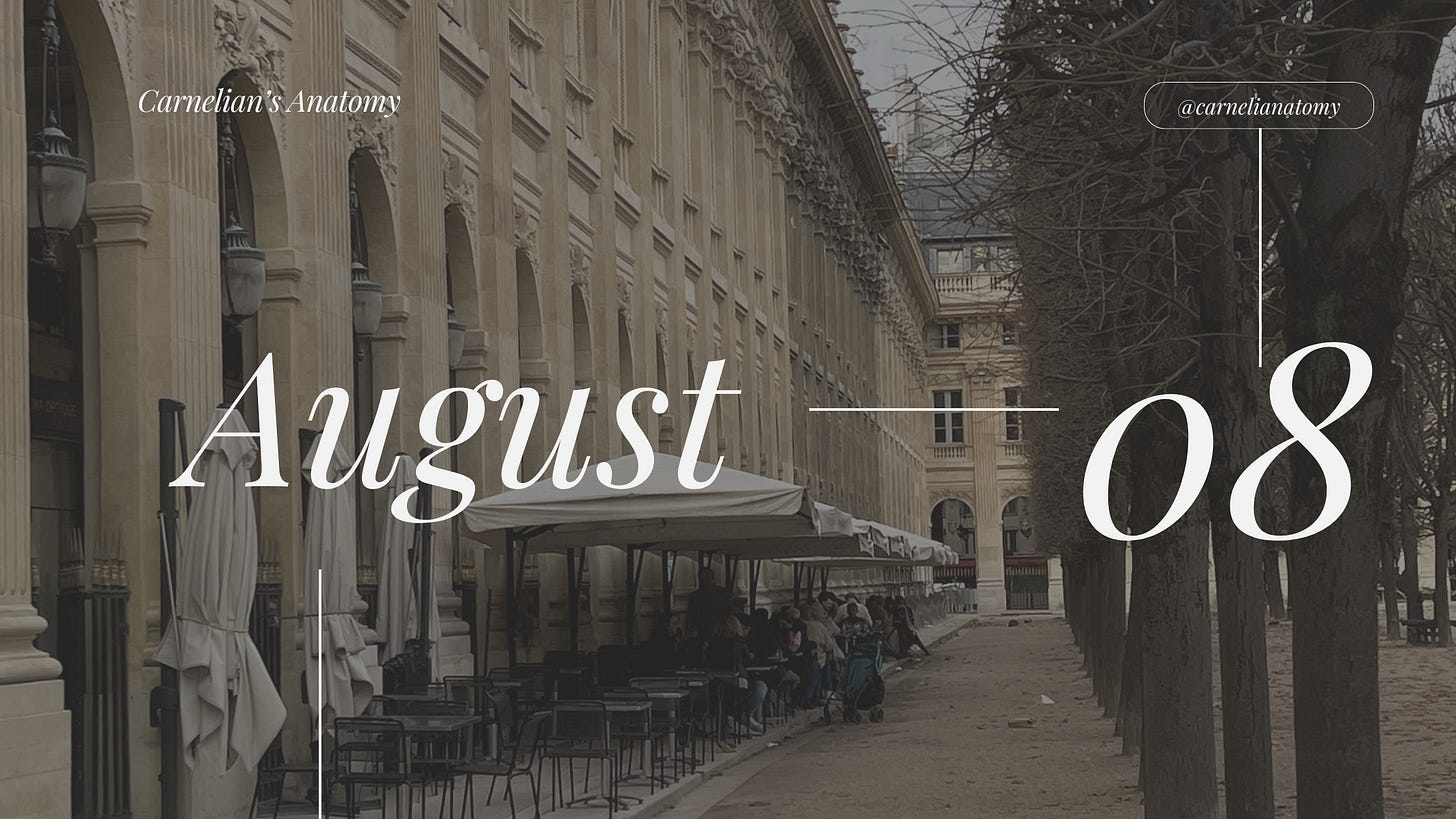 Pictured is a banner for the month of August. The top layer is the numerical month and our publication user name. The background are Parisian style restaurants in a row coming from the diagonal of the image. On the right is a dirt pathway paved by trees in what appears to be their winter stage.