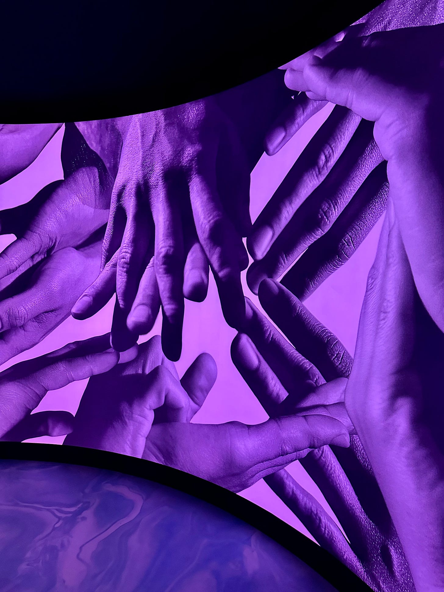 Photo of a large scale artwork showing interlocking fingers in black and white on a backlit purple background.