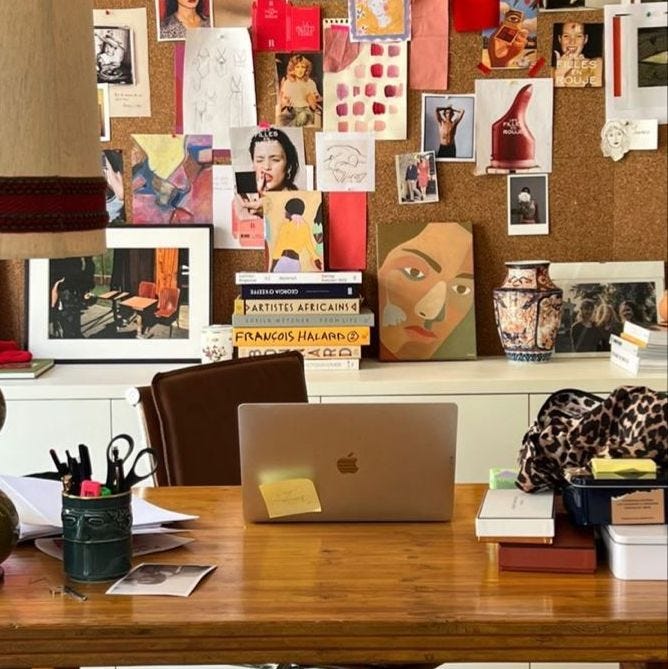 This may contain: a wooden desk topped with a laptop computer sitting next to a wall covered in pictures