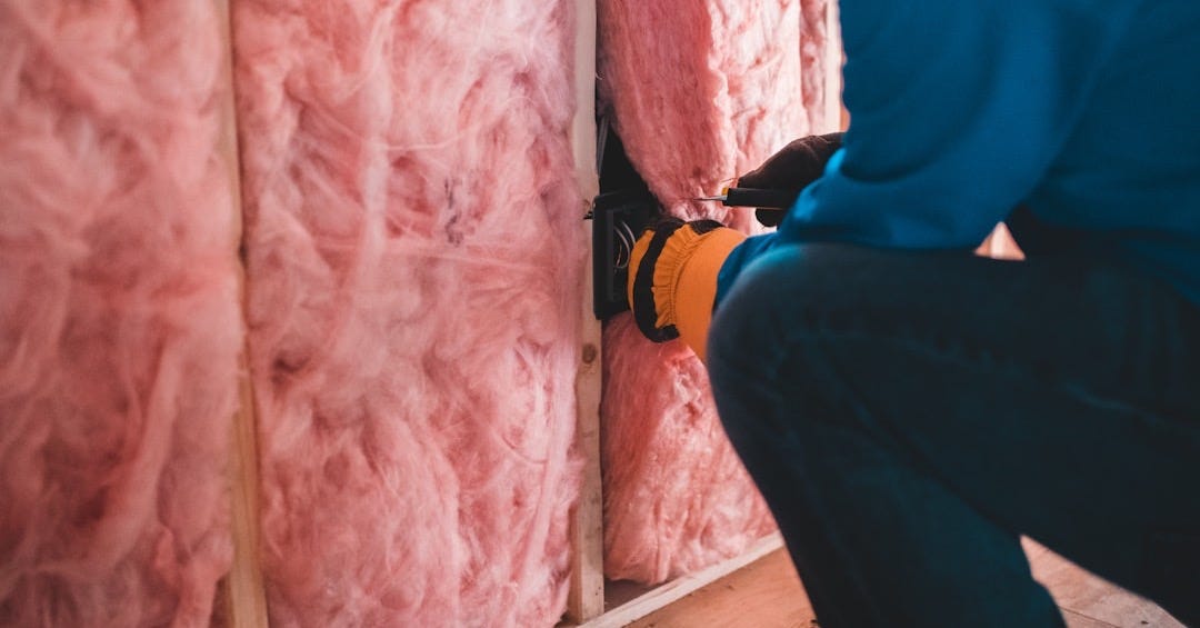 A person in a blue shirt installing electrical wiring in pink fiberglass wall insulation