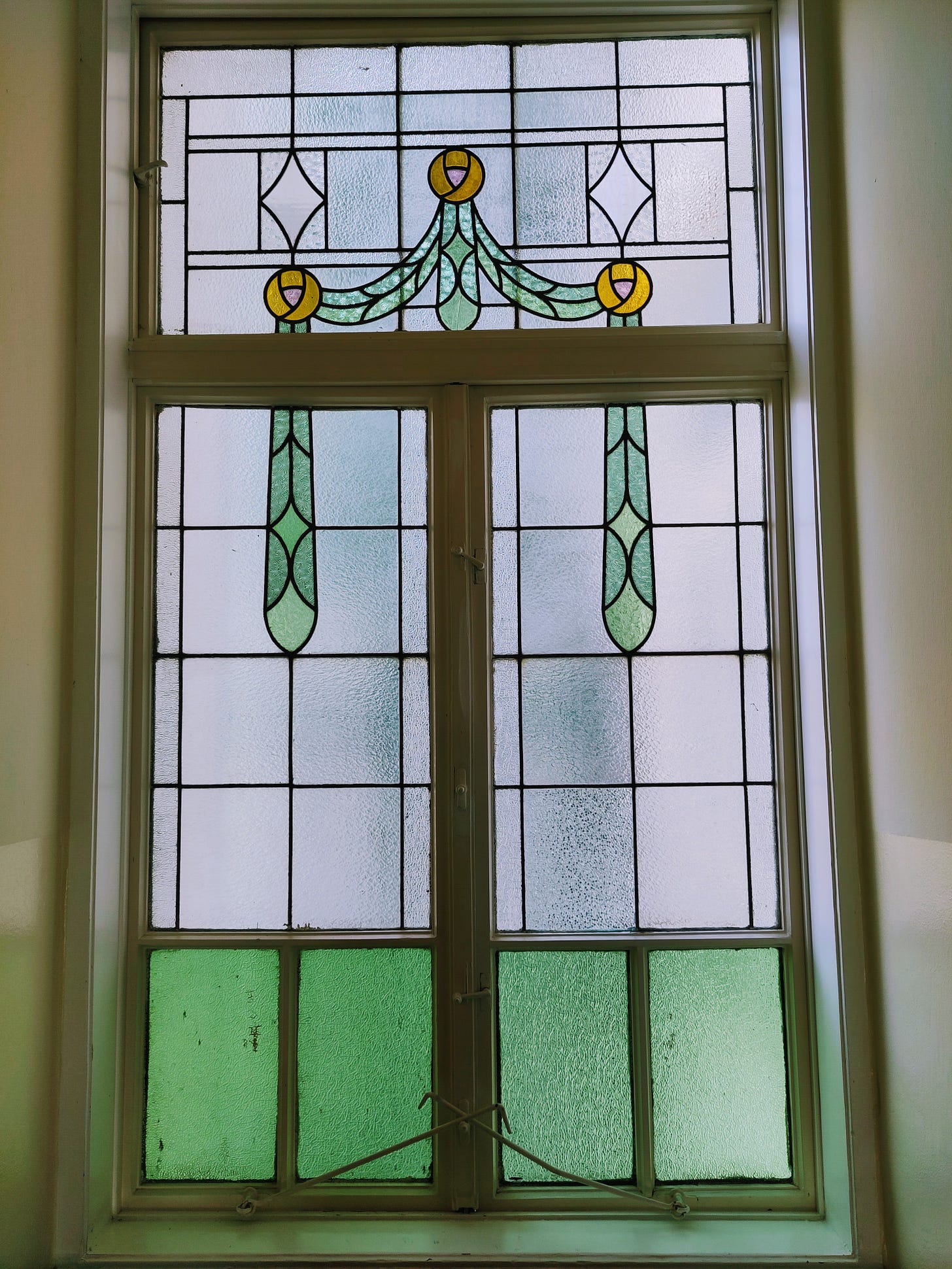 The photo shows a stained glass window. The design is simple with some green glass and yellow, but it looks beautiful.