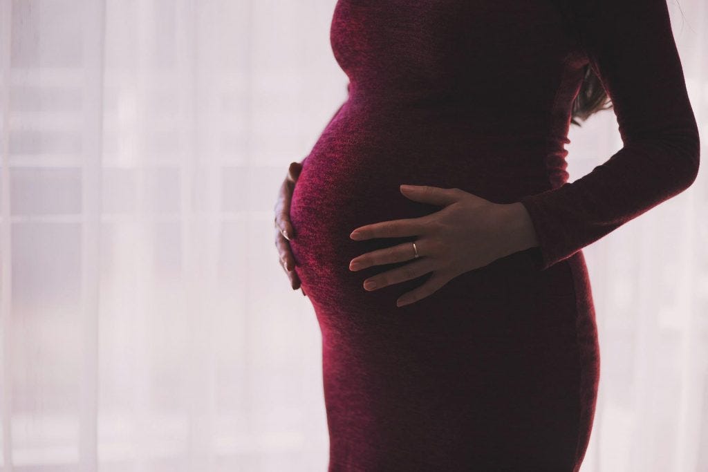 Up close view of a pregnant woman in a dark red dress with her hands on her abdomen Up close view of a pregnant woman in a dark red dress with her hands on her abdomen
