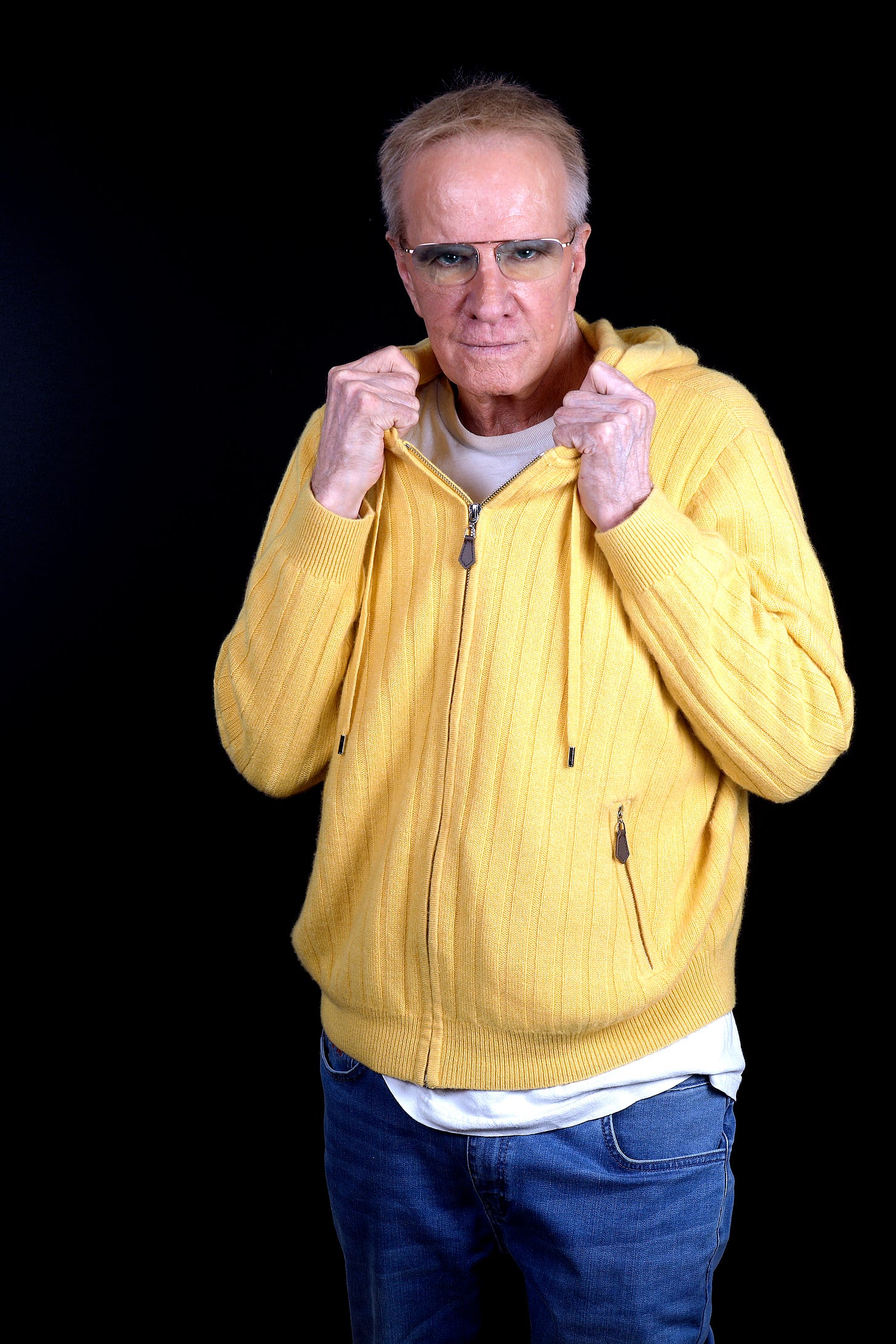 Actor Christophe Lambert in a yellow zippered hoodie and glasses.