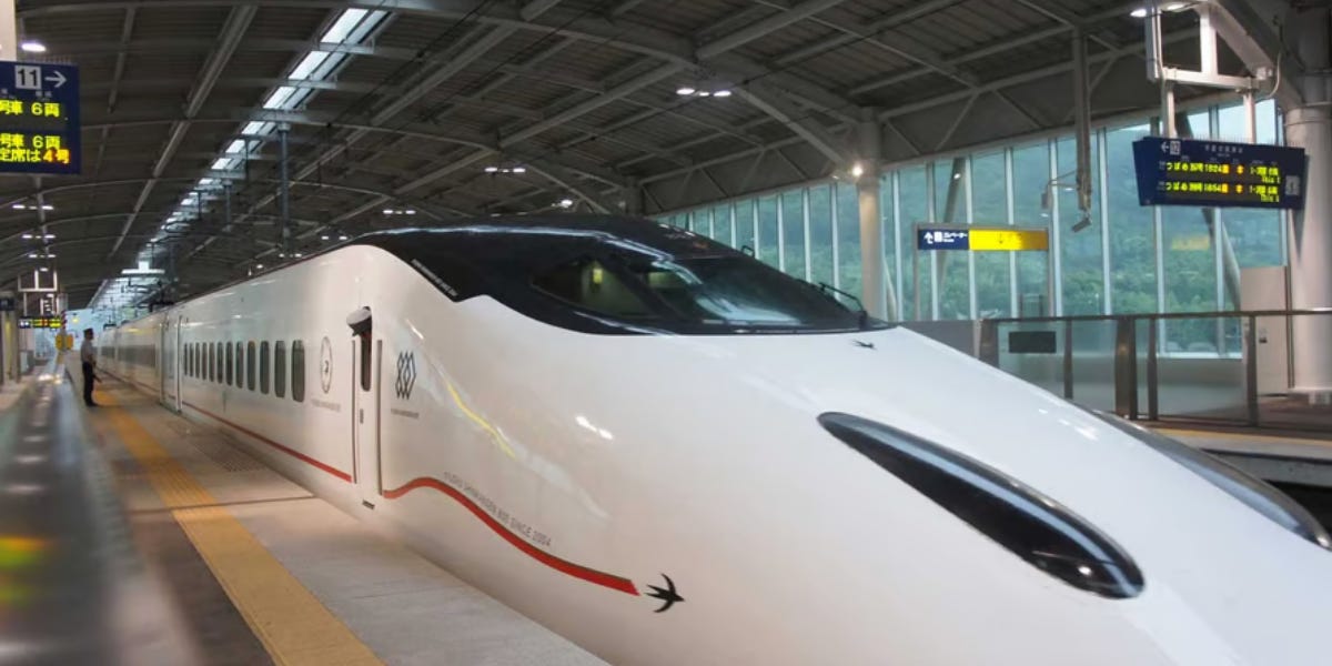 A white Kyushu Shinkansen bullet train with its distinctive aerodynamic nose and red accent stripe is stopped at a station platform.