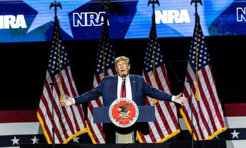 man in a suit with arms outstretched in front of american flags