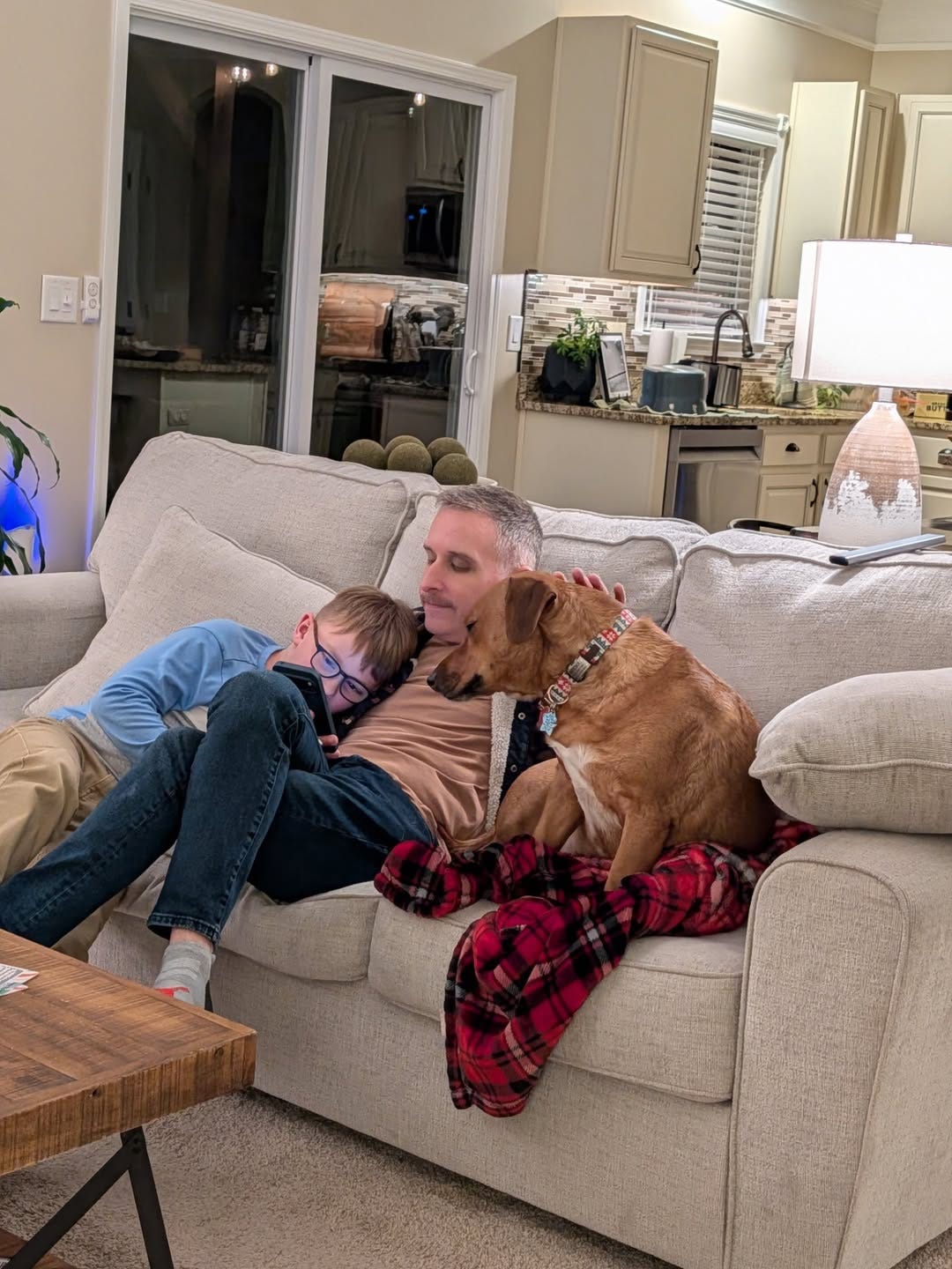 man with his son and rescue dog sitting on tan coach with red plaid blanket man with his son and rescue dog sitting on tan coach with red plaid blanket