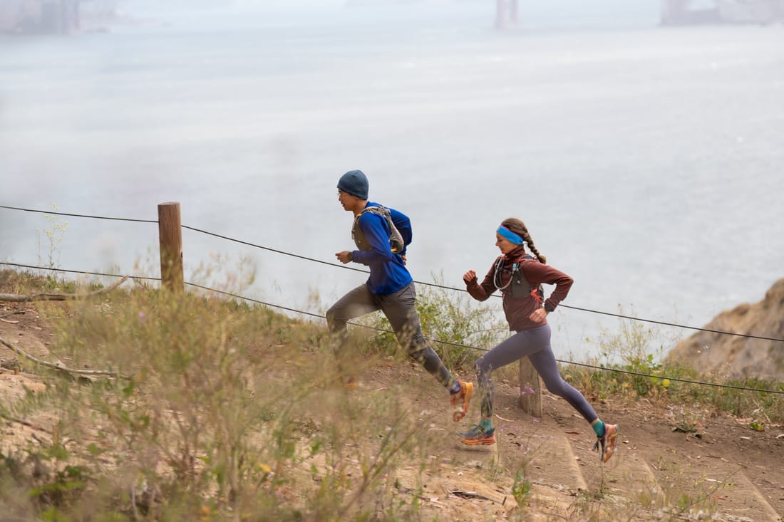 Two trail runners jog up a hill along a shoreline. 