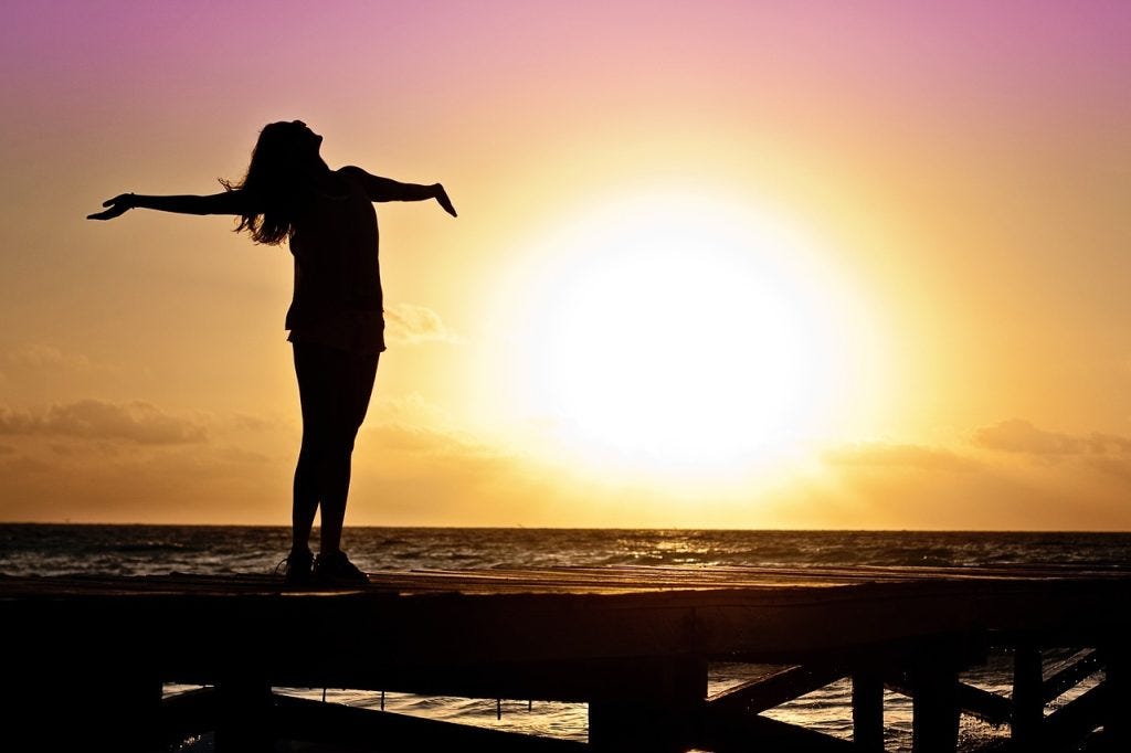 Darkened silhouette of a woman standing in the evning on a pier at sunset, her arms spread out in joy, her long hair flowing behind her. Darkened silhouette of a woman standing in the evning on a pier at sunset, her arms spread out in joy, her long hair flowing behind her.
